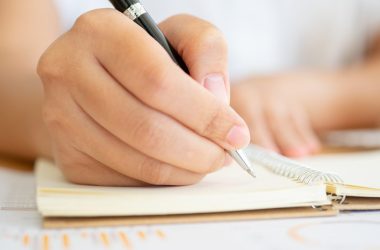 Close shot of businesswoman hands holding a pen writing something on the paper on the foreground in office. Recording concept